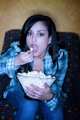 Pretty Hispanic woman with popcorn watching television