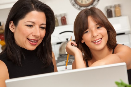 Attractive Hispanic Mother and Mixed Race Daughter in the Kitchen using the Laptop Computer Together.